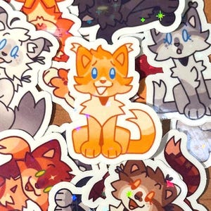 Op de afbeelding: Een verzameling kleurrijke kattenstickers in verschillende poses. De stickers bevatten cartoon-achtige illustraties van katten in tinten oranje, bruin, grijs en wit. Sommige stickers hebben een holografisch effect, wat een glinsterende kwaliteit toevoegt.