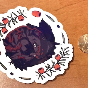 Pode incluir: Um autocolante com uma ilustra&ccedil;&atilde;o estilizada de um lobo enrolado em tons de roxo e vermelho, rodeado por uma borda branca com bagas vermelhas e folhas verdes. Uma moeda est&aacute; ao lado para compara&ccedil;&atilde;o de tamanho.