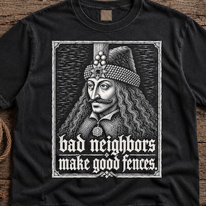 May include: A black short-sleeve t-shirt featuring a white graphic print of a historical figure wearing a jeweled hat and long hair. Below the portrait, the text reads, "bad neighbors make good fences." The design is enclosed in a rectangular border.