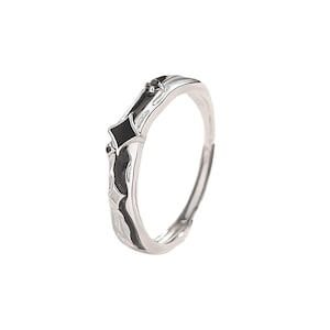 K&ouml;nnte beinhalten: Ein silberner Ring mit schwarzen Emaille-Akzenten. Der Ring hat ein geometrisches Design mit zwei schwarzen Diamantformen und einem kleinen schwarzen Stein. Das Band hat ein strukturiertes Muster und ist verstellbar.