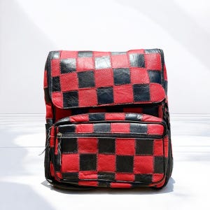 May include: A red and black checkered backpack with a flap closure and a front zippered pocket. The backpack is made of a patchwork design with a black zipper and black trim.