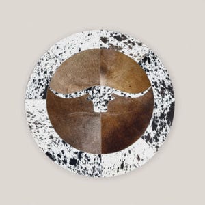 Peut inclure: Tapis rond en peau de vache avec un motif central de silhouette de longhorn. Le tapis présente un design patchwork avec des sections marron, beige et blanches, et des mouchetures noires. Esthétique rustique et d'inspiration western.