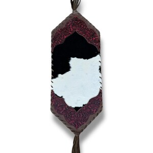 May include: A black and white cowhide table runner with a burgundy embroidered border and tassels.