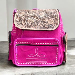 May include: A hot pink backpack with a floral tooled leather flap. The backpack has a front pocket with a zipper and white stitching details. The sides have pockets and the straps are adjustable.