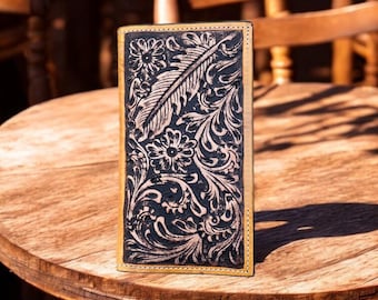 May include: A black leather wallet with a tooled floral design. The wallet is closed and sitting on a wooden table.