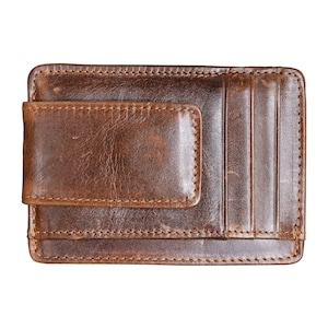 May include: A brown leather wallet with a money clip and card slots. The wallet is rectangular and has a distressed appearance. The stitching is visible around the edges of the wallet and the money clip.