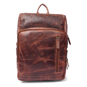 May include: A brown leather backpack with a top handle and multiple zippered compartments. The front pocket features a vertical zipper and the text "MINOR LEATHER". The bag has a distressed, textured appearance.