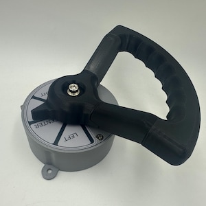 Può includere: Un pomello di controllo grigio e nero con etichette direzionali. Il pomello ha una base circolare con le parole "CENTER", "LEFT" e "RIGHT". Una maniglia nera è attaccata alla parte superiore.