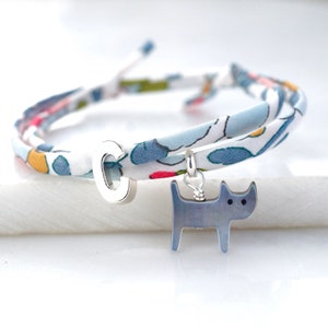 Puede incluir: Un brazalete de tela floral azul y blanco con un dije de plata de un perro y la letra C.