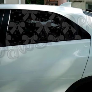Pode incluir: Um carro branco com um vidro traseiro com um padrão de laço preto. Os laços são cinzentos e dispostos sobre um fundo preto com pequenos pontos brancos. A carroçaria do carro é de um branco brilhante.