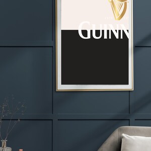 K&ouml;nnte beinhalten: Gerahmtes Wandbild mit dem Guinness-Logo. Das Kunstwerk hat einen goldenen Rahmen und ein zweifarbiges Design mit einem cremefarbenen oberen Bereich und einem schwarzen unteren Bereich. Das Guinness-Logo und der Text sind in Wei&szlig; und Gold gehalten.