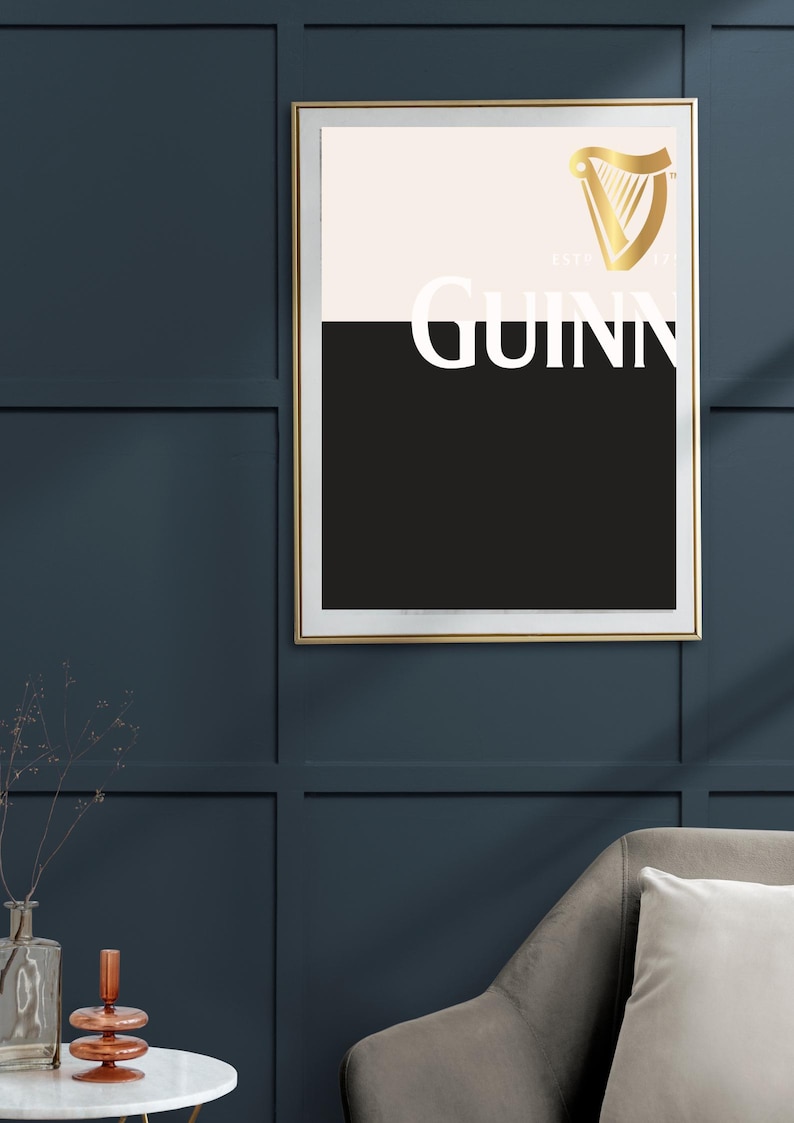 K&ouml;nnte beinhalten: Gerahmtes Wandbild mit dem Guinness-Logo. Das Kunstwerk hat einen goldenen Rahmen und ein zweifarbiges Design mit einem cremefarbenen oberen Bereich und einem schwarzen unteren Bereich. Das Guinness-Logo und der Text sind in Wei&szlig; und Gold gehalten.