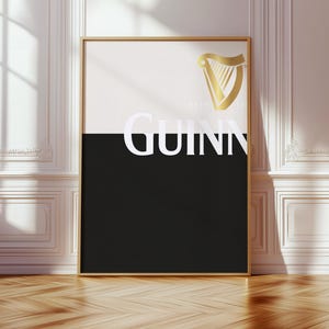 K&ouml;nnte beinhalten: Ein gerahmtes Poster mit goldenem Rand mit dem Guinness-Logo. Die obere H&auml;lfte ist wei&szlig;, die untere schwarz, mit dem Wort "GUINNESS" in Wei&szlig;. Ein goldenes Harfenlogo befindet sich in der oberen rechten Ecke. Das Poster lehnt an einer wei&szlig;en Wand.