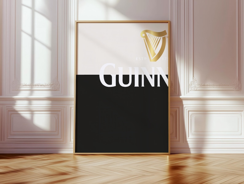 K&ouml;nnte beinhalten: Ein gerahmtes Poster mit goldenem Rand mit dem Guinness-Logo. Die obere H&auml;lfte ist wei&szlig;, die untere schwarz, mit dem Wort "GUINNESS" in Wei&szlig;. Ein goldenes Harfenlogo befindet sich in der oberen rechten Ecke. Das Poster lehnt an einer wei&szlig;en Wand.