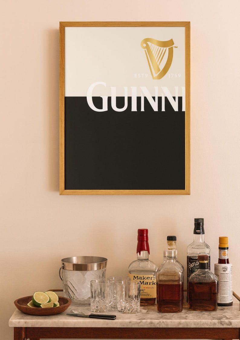 K&ouml;nnte beinhalten: Gerahmtes Guinness-Poster mit goldenem Harfenlogo und Markennamen in Wei&szlig;. Dar&uuml;ber ein Barwagen mit Spirituosenflaschen, einem Eisk&uuml;bel, Gl&auml;sern und einer Holzschale mit Limetten.