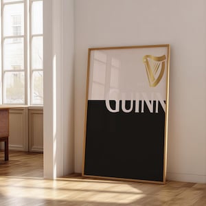 May include: A framed poster featuring the Guinness logo. The top half is white, the bottom black, with the word "GUINNESS" in white. A gold harp logo is in the upper right corner. The frame is gold.