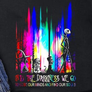 Könnte beinhalten: Schwarzes T-Shirt mit einer farbenfrohen Grafik mit Figuren und dem Text "INTO THE DARKNESS WE GO TO LOSE OUR MINDS AND FIND OUR SOULS." Das Shirt wird mit blauen Jeans und schwarzen Leinenschuhen gezeigt.