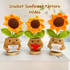 May include: Three crochet sunflowers with yellow petals and brown centers sit in brown pots with smiling faces. Each pot holds a green leaf and a sunflower. One pot holds a red heart, and the others hold cards with text.