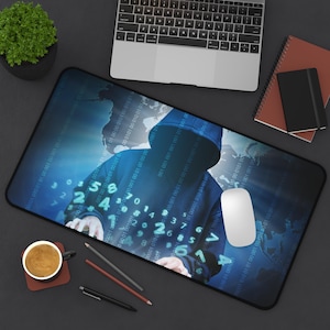 Peut inclure: Un tapis de souris rectangulaire noir avec un motif d'art numérique d'une personne dans un sweat à capuche bleu, avec du code binaire et des chiffres. Une souris blanche, un ordinateur portable, une tasse de café et des articles de papeterie sont sur une surface sombre.