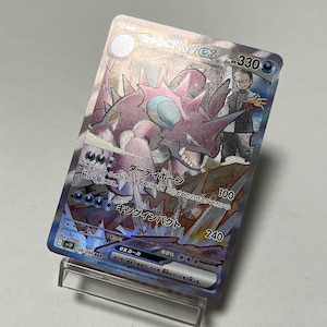 Puede incluir: Una carta coleccionable Pokémon holográfica con un Nidoking morado con un cuerno rosa y una ilustración de entrenador. La carta tiene texto japonés y el número 330. La carta se muestra en un soporte de plástico transparente.