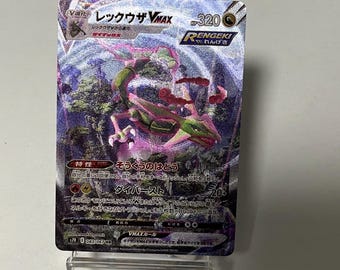 May include: A Pokémon trading card featuring a green and pink dragon-like creature with the Japanese text "レックウザ VMAX". The card has a holographic background with the text "RENGKI" and "320". The card is displayed on a clear plastic stand.