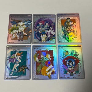 Può includere: Sei carte collezionabili olografiche con testo giapponese e illustrazioni colorate. Le carte presentano vari personaggi e creature. Le carte provengono da un gioco di carte collezionabili, con la parola "TRAINER'S" visibile su alcune carte.