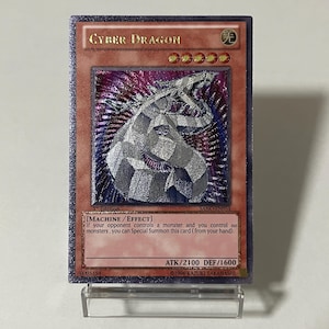 Puede incluir: Una carta de juego Cyber Dragon con una ilustración de dragón plateado sobre un fondo morado y plateado. La tarjeta tiene el texto "CYBER DRAGON" en la parte superior y "ATK/2100 DEF/1600" en la parte inferior.