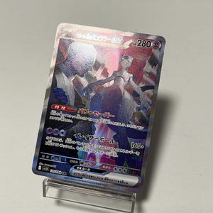 Puede incluir: Una tarjeta coleccionable Pokémon holográfica con un personaje Mewtwo morado y blanco y texto japonés. La tarjeta tiene un borde plateado y se muestra en un soporte transparente. La tarjeta tiene 280 HP.