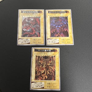 Puede incluir: Tres cartas coleccionables con texto japonés e ilustraciones de criaturas fantásticas. Las cartas presentan dragones y otros seres míticos en tonos dorados, rojos y morados.