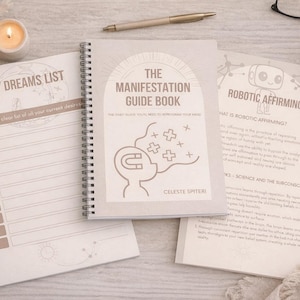 May include: A collection of stationery items including a spiral-bound notebook titled "The Manifestation Guide Book" and a "My Dreams List" notepad. A lit candle, pen, and coffee cup are also present. The book cover features a graphic of a head with a magnet and plus signs.