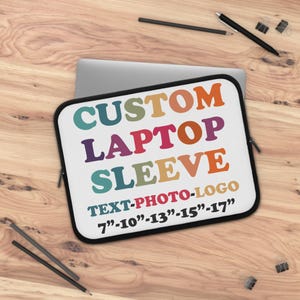Puede incluir: Una funda blanca para portátil con el texto "CUSTOM LAPTOP SLEEVE" en letras coloridas. El texto "TEXT-PHOTO-LOGO" está debajo, con opciones de tamaño de 17.78 cm a 43.18 cm. La funda está sobre una superficie de madera.