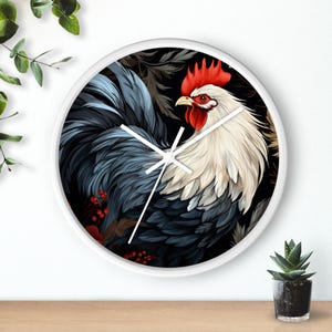 May include: A white-framed wall clock featuring a detailed illustration of a rooster. The rooster has red comb and wattle, white and blue feathers, set against a black floral background. The clock hands are white.