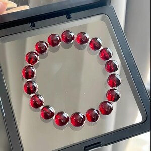 May include: A red gemstone bracelet with round beads. The bracelet is displayed in a black velvet box.