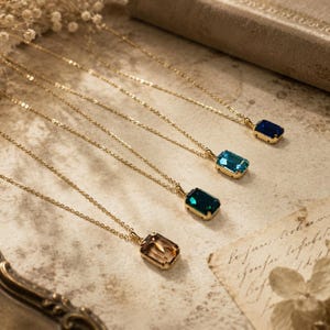 Pode incluir: Quatro colares com correntes finas em tom dourado, cada um com um pendente retangular facetado. Os pendentes são de cor champanhe claro, verde esmeralda profundo, azul turquesa brilhante e azul marinho escuro, em metal dourado.