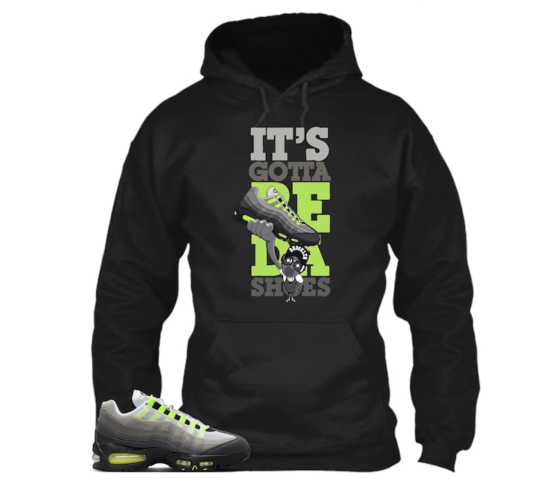 May include: Black hooded sweatshirt with the text "IT'S GOTTA BE DA SHOES" in gray and green. The graphic features a cartoon character holding a sneaker. A gray and neon green sneaker is in the lower left corner.
