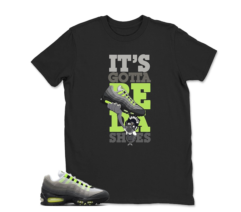 May include: Black t-shirt with the text "IT'S GOTTA BE DA SHOES" in gray and neon green. The graphic features a cartoon character holding a sneaker. A matching gray and neon green sneaker is in the foreground.