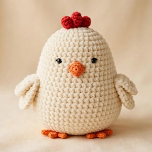 May include: A cream-colored crochet chicken plush toy featuring a small red comb on top of its head, a bright orange beak, two black bead eyes, and two orange feet. The body is round and textured with visible yarn stitches throughout the design.