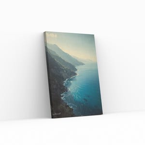 Può includere: Stampa su tela raffigurante un paesaggio costiero. L'opera mostra una vista drammatica di una costa frastagliata dove le montagne incontrano il mare. L'acqua è di un turchese vibrante, in contrasto con le scogliere scure. Il cielo è azzurro.