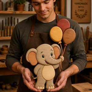 May include: A wooden cutout of a smiling elephant holding three balloons in red, yellow, and brown. The elephant is light brown with darker brown ears and a lighter tan belly. The balloons are attached to the elephant's trunk with thin wooden stems.