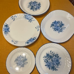May include: Set of five white ceramic plates with blue floral designs. The plates include a large dinner plate, a smaller dinner plate, a salad plate, and two bowls.