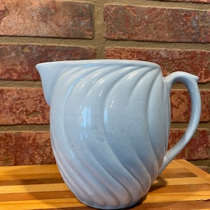 May include: A light blue ceramic pitcher with a swirl design. The pitcher has a handle and a spout.