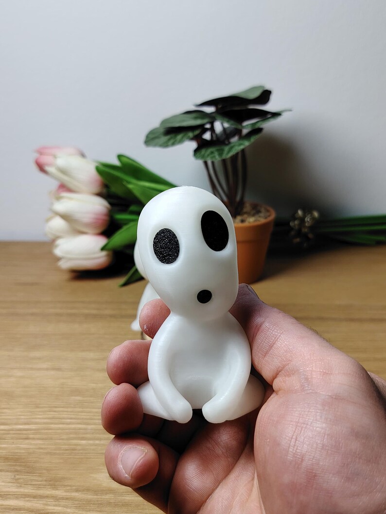 May include: A white, sitting figurine with black eyes and a small mouth. The figurine is made of a smooth, matte material and has a rounded shape.