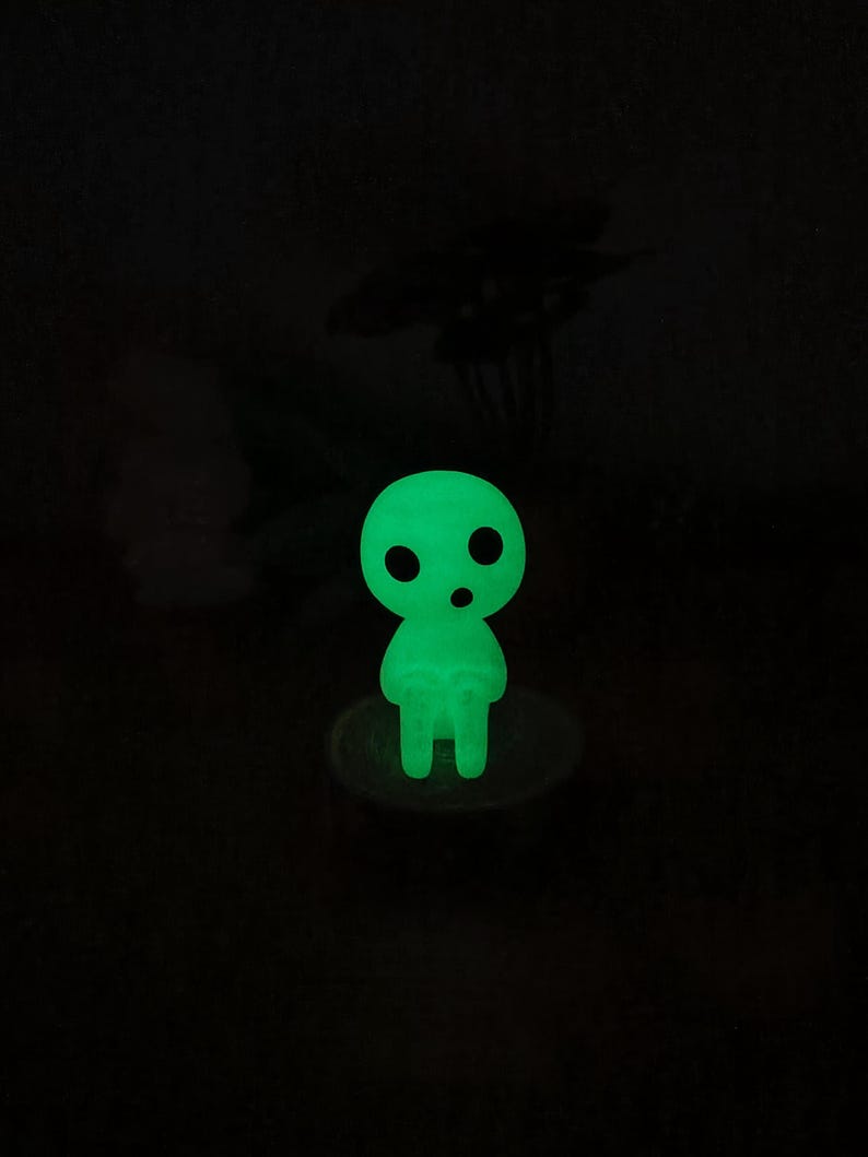 May include: A green glow-in-the-dark figurine of a small, round, humanoid character with two eyes and a mouth. The figurine is standing on a small, round base.