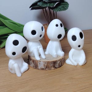 K&ouml;nnte beinhalten: Vier wei&szlig;e Figuren mit schwarzen Augen, die Waldgeistern &auml;hneln, sind auf einer Holzoberfl&auml;che angeordnet. Zwei der Figuren sitzen auf einem kleinen Holzscheit, w&auml;hrend die anderen beiden auf der Oberfl&auml;che sitzen.