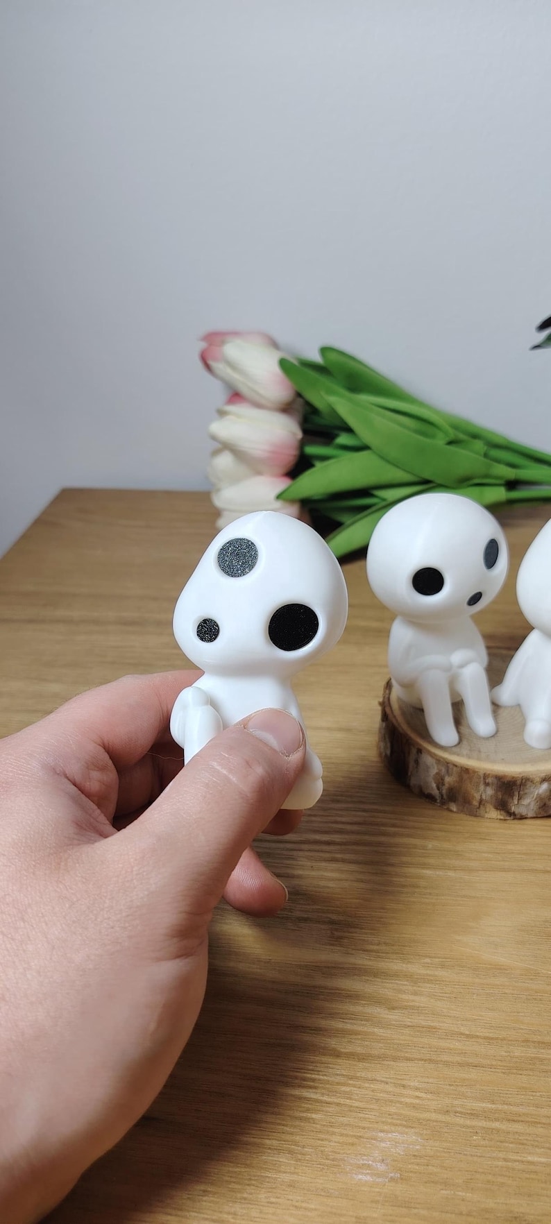 K&ouml;nnte beinhalten: Drei wei&szlig;e Figuren mit schwarzen Augen und Flecken, die an Figuren aus dem Film "Mein Nachbar Totoro" erinnern. Die Figuren stehen auf einem Holzsockel, eine Figur wird in der Hand gehalten.