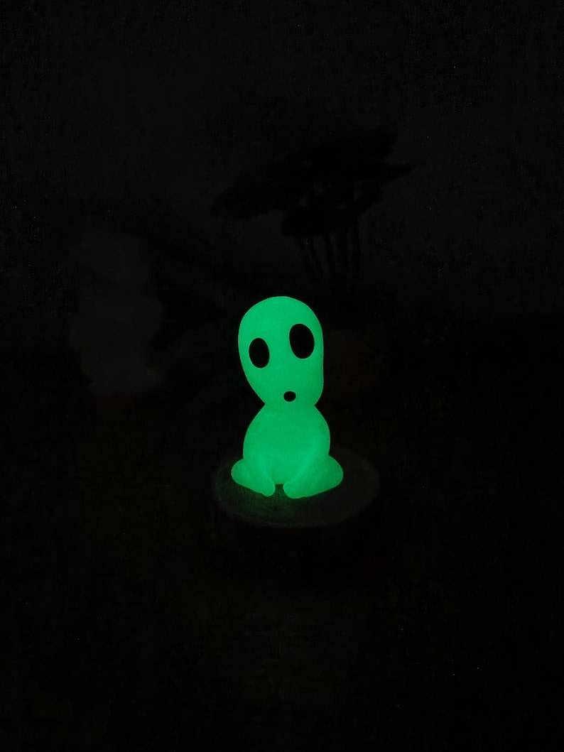 May include: A green glow-in-the-dark figurine of a character from the movie 'My Neighbor Totoro'. The figurine is sitting on a small wooden base.