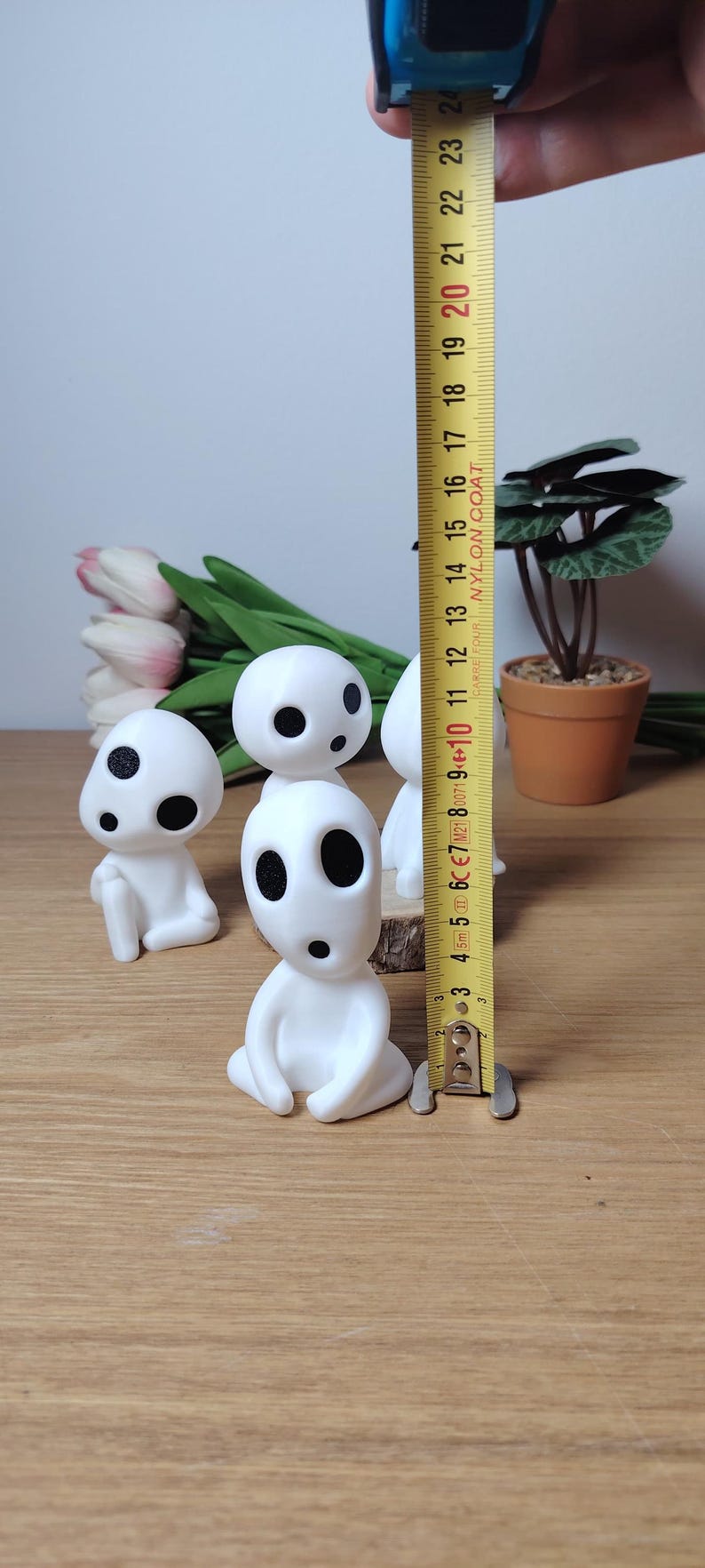 K&ouml;nnte beinhalten: Vier wei&szlig;e Figuren mit schwarzen Augen und M&uuml;ndern, die an Figuren aus dem Animationsfilm "Mein Nachbar Totoro" erinnern. Die Figuren sitzen auf einer Holzoberfl&auml;che, im Hintergrund befindet sich ein Ma&szlig;band.