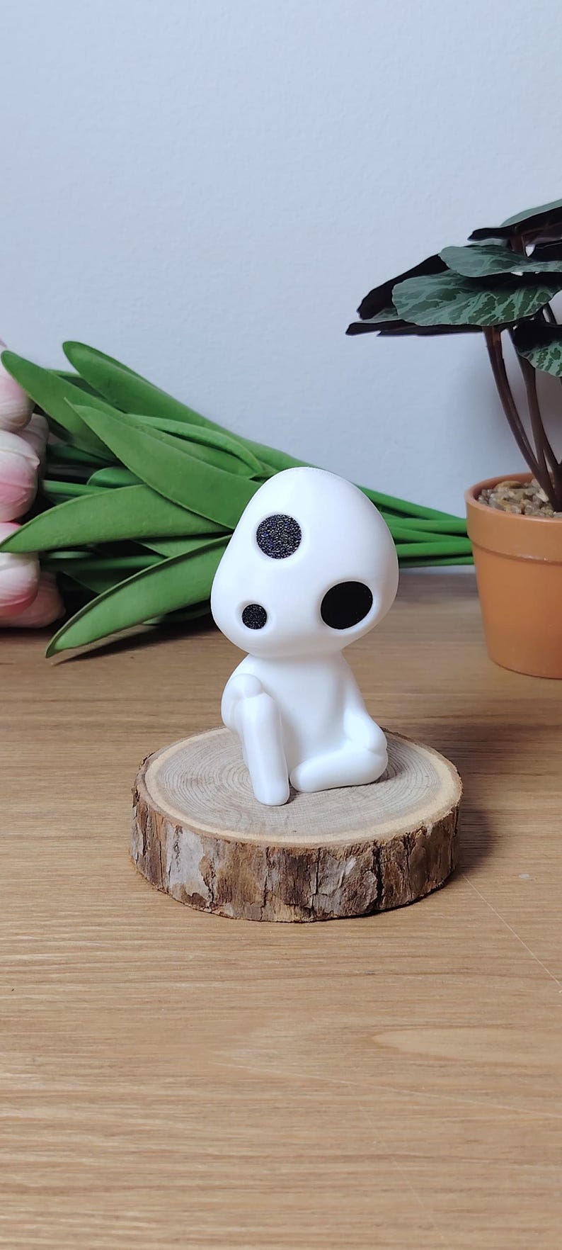 K&ouml;nnte beinhalten: Wei&szlig;e Figur eines Charakters mit zwei schwarzen Augen, sitzend auf einer Holzscheibe. Die Figur ist ein beliebter Charakter aus dem Animationsfilm 'Howls bewegliches Schloss'.