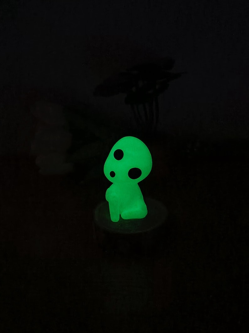 May include: A green glow-in-the-dark figurine of a mushroom-like creature with black dots. The figurine is sitting on a small wooden base.
