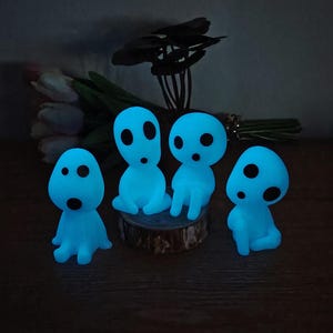 May include: Four blue glowing figurines with round eyes and mouths, sitting on a wooden surface. The figurines are reminiscent of the characters from the animated film "My Neighbor Totoro".